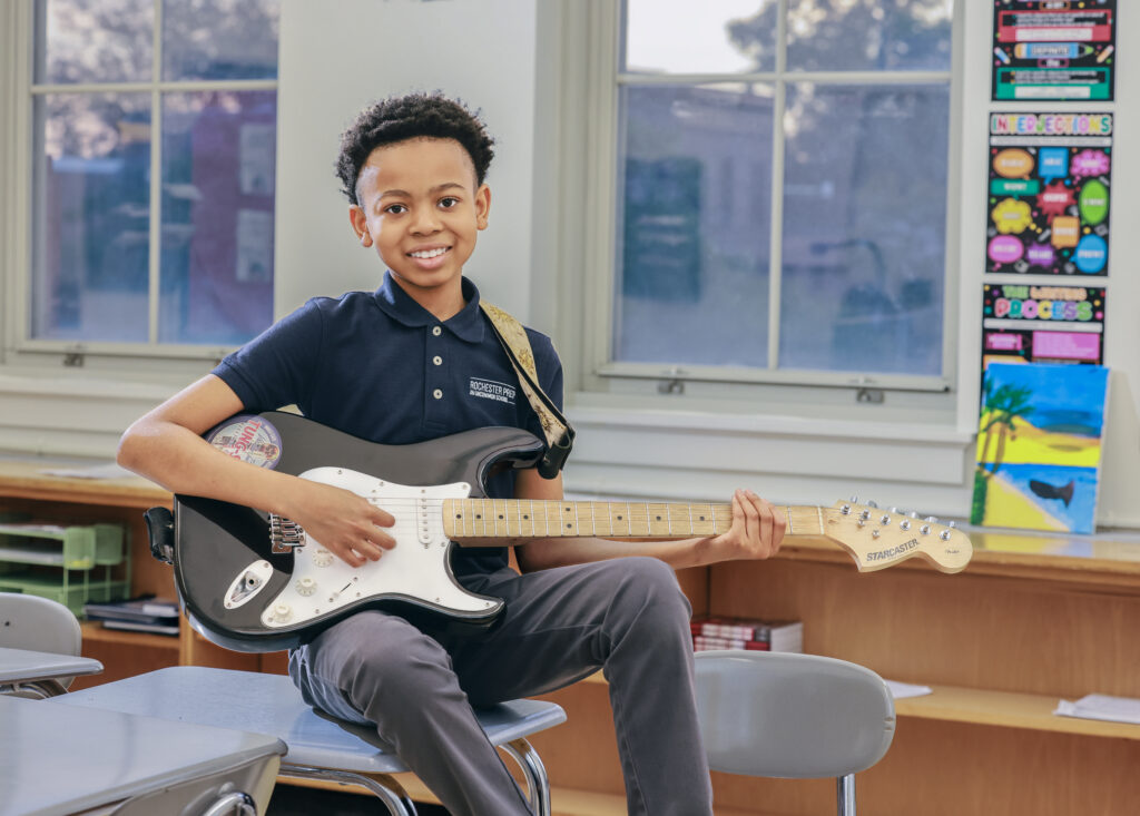 student sitting on desk with an electric guitar